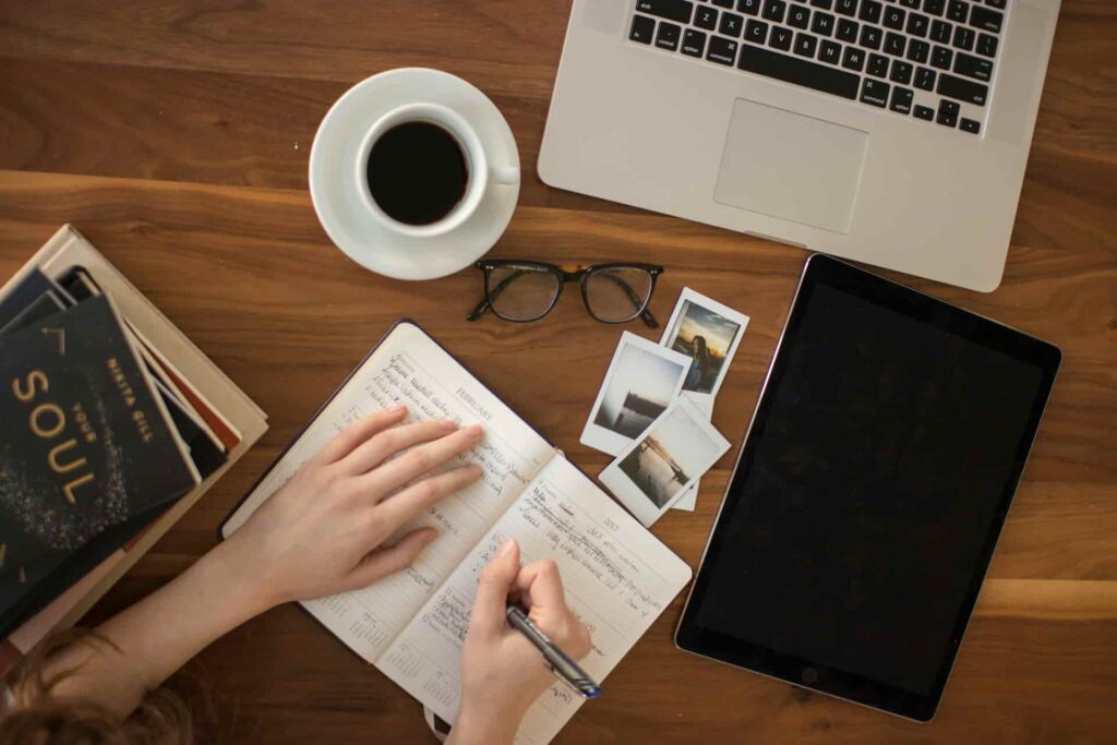 Personne écrivant dans un carnet entourée d'ordinateur et café symbolisant l'apprentissage continu