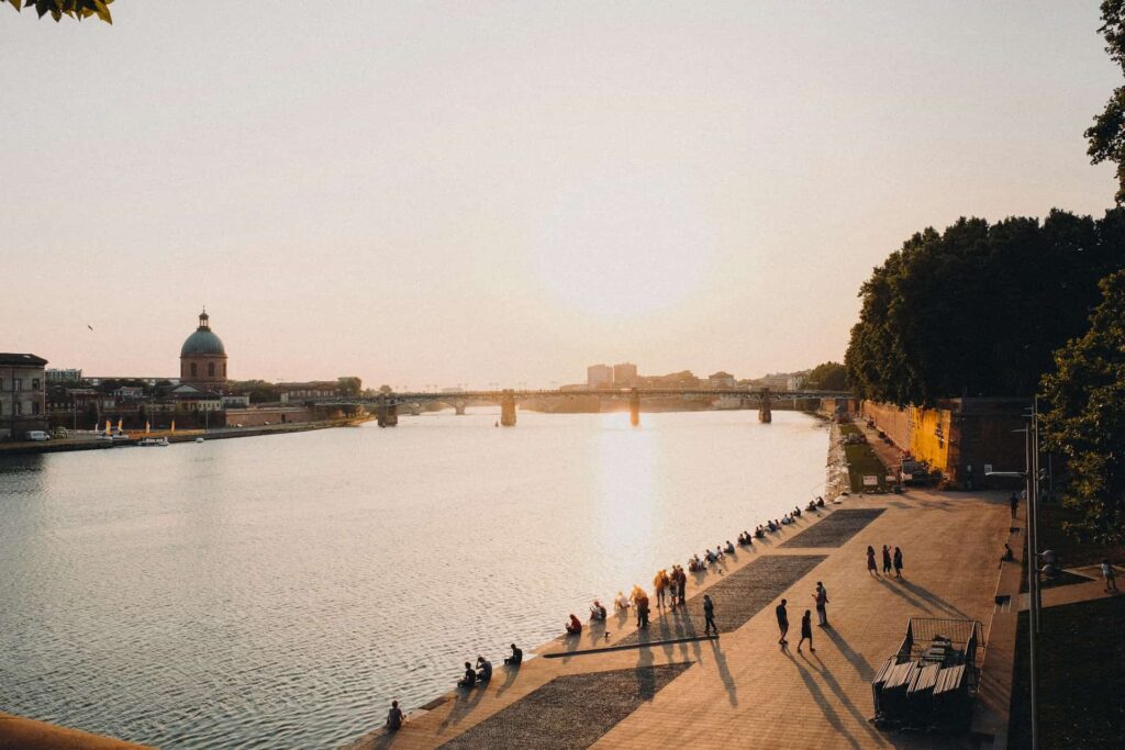 Vue sur la Garonne à Toulouse au coucher du soleil, avec le dôme de La Grave et les quais bordés d’arbres.